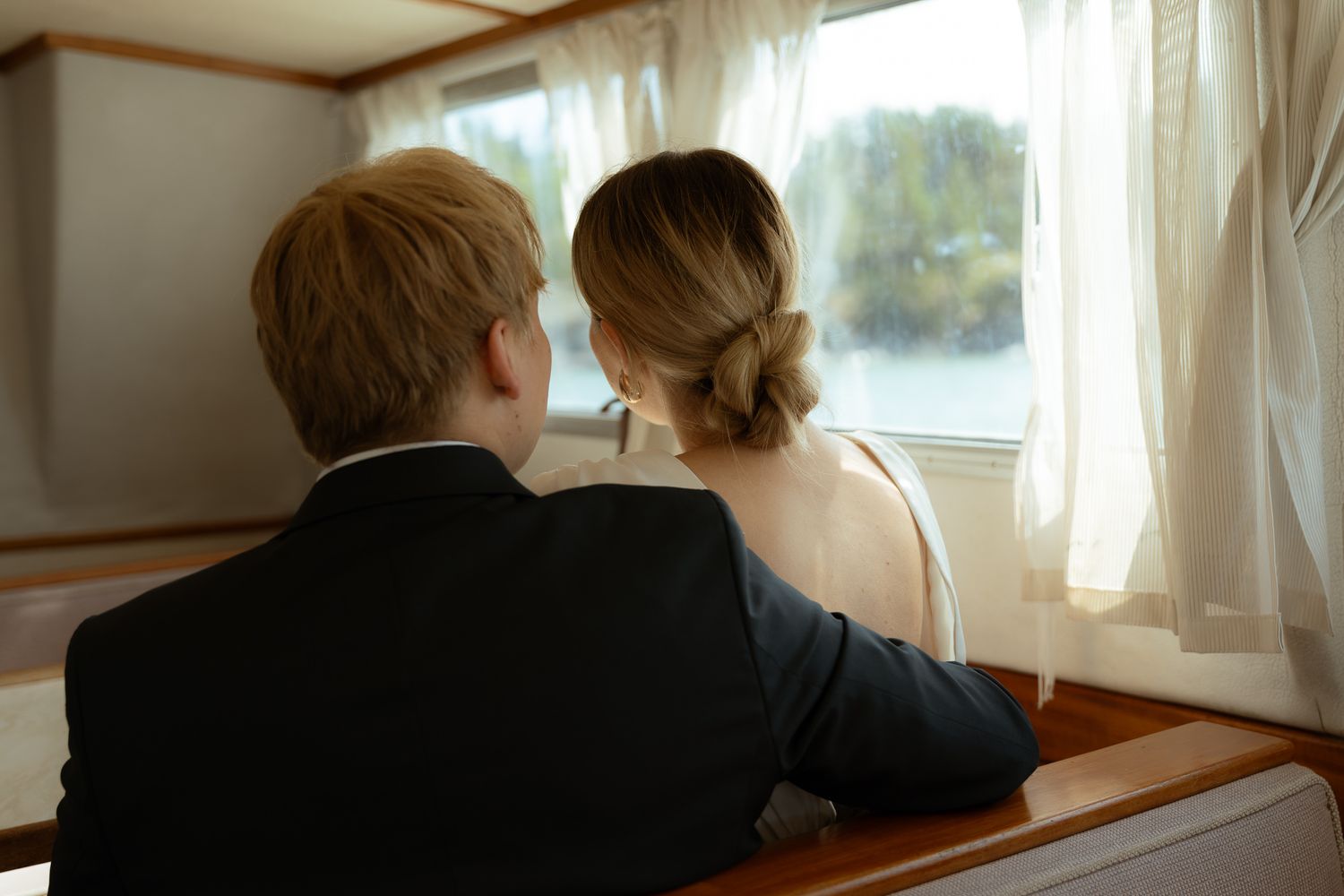 A couple in formal attire sits together looking out a window on a boat or ship.