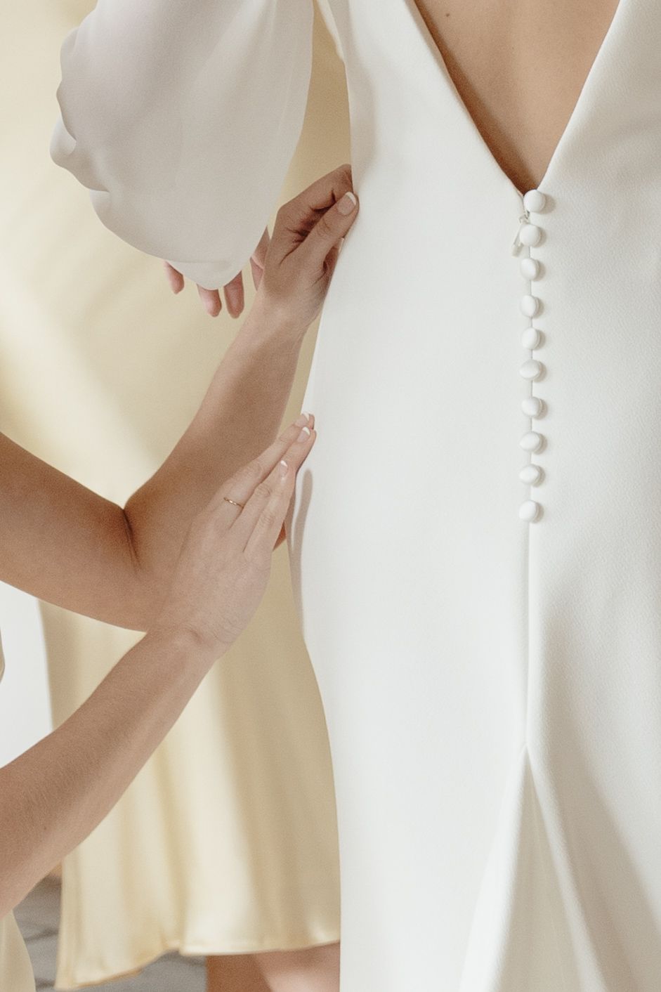 Detail shot of delicate button closures on a white wedding dress being adjusted.