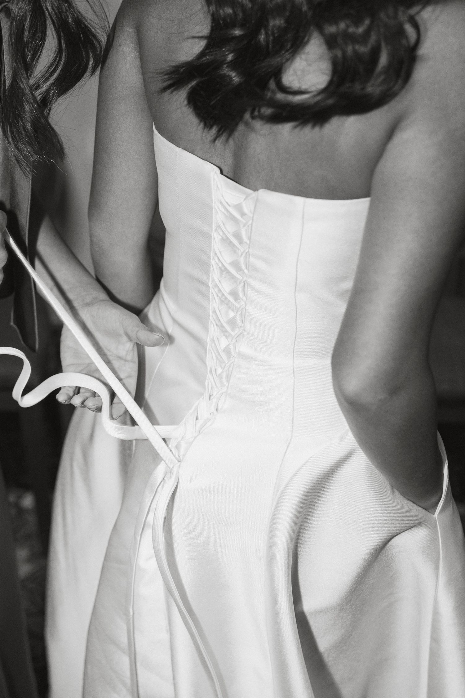 Back view of a white corset wedding dress showing intricate lacing detail in black and white photography.