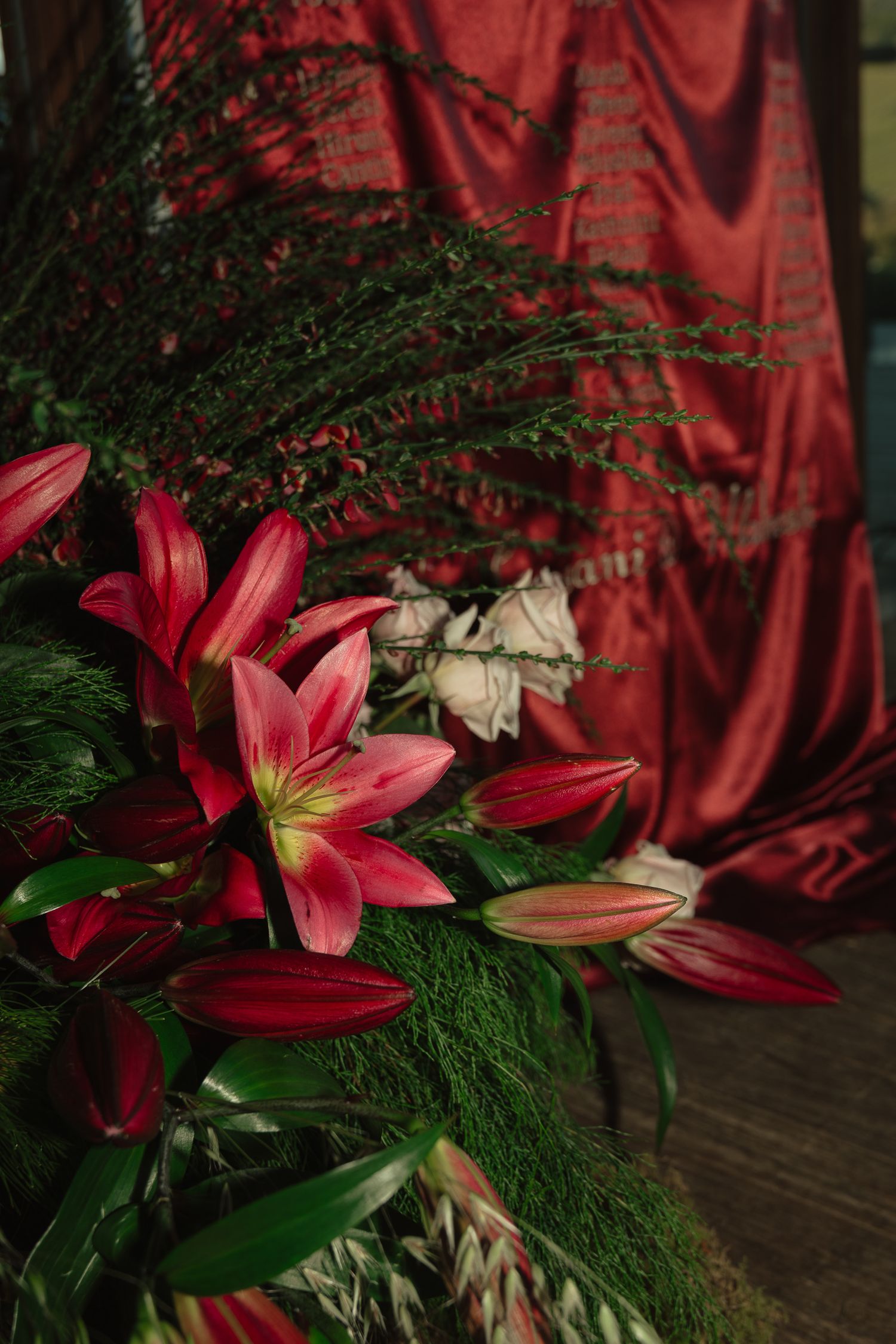 Pink lilies and greenery arranged against a deep red velvet backdrop create an elegant floral display.