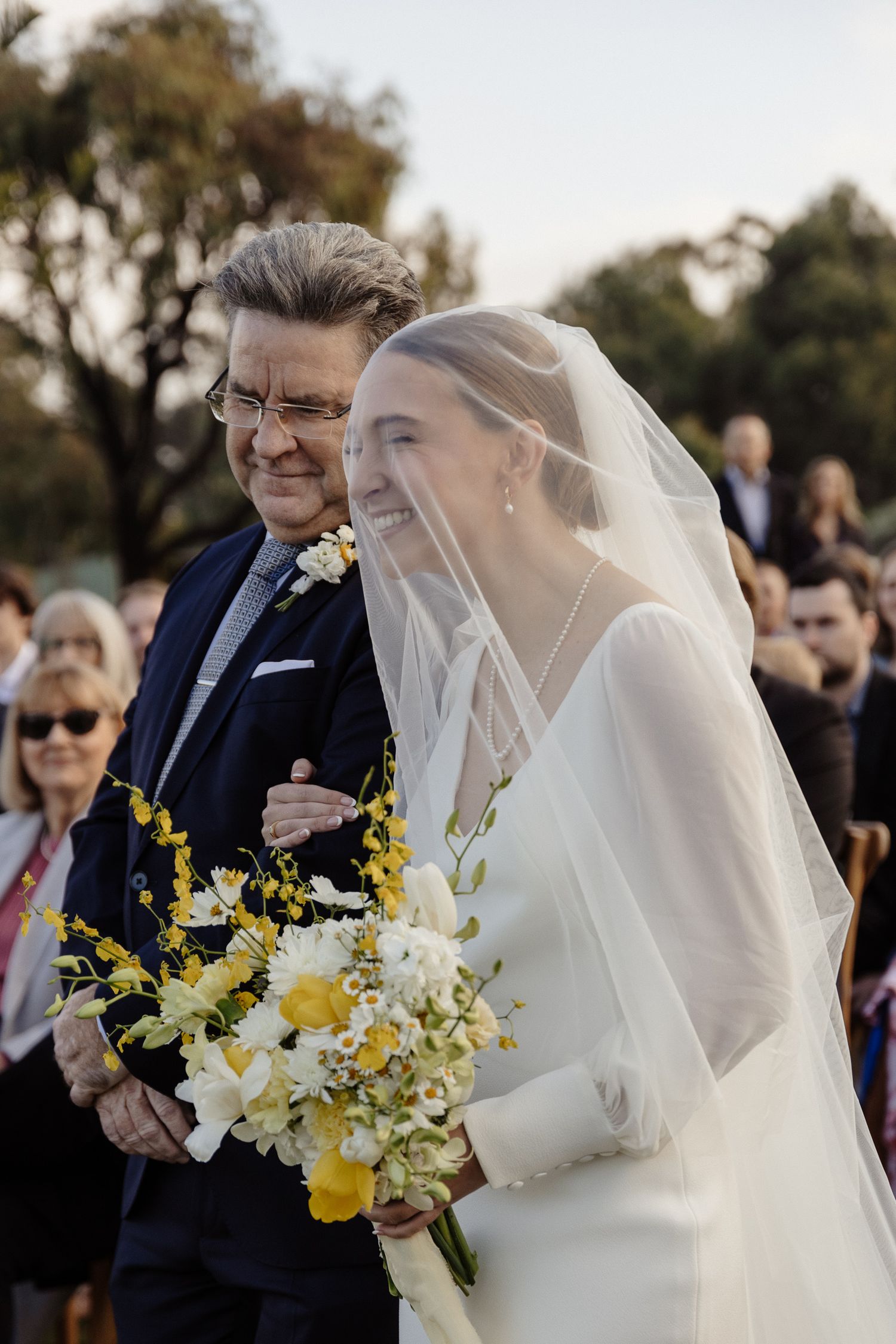 Traditional outdoor wedding ceremony processional with yellow and white bouquet.