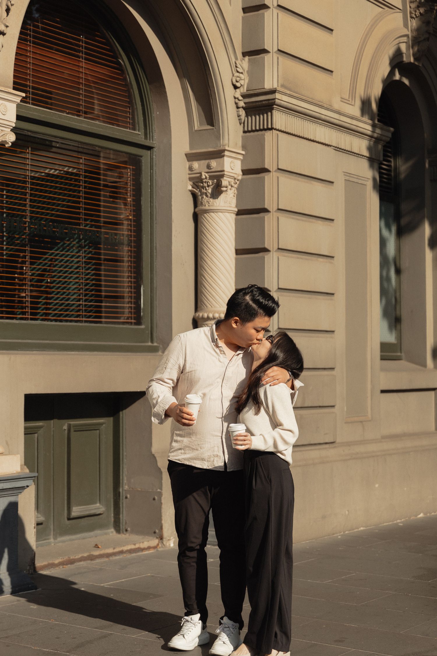 A couple shares an intimate moment under classical architecture with arched windows.