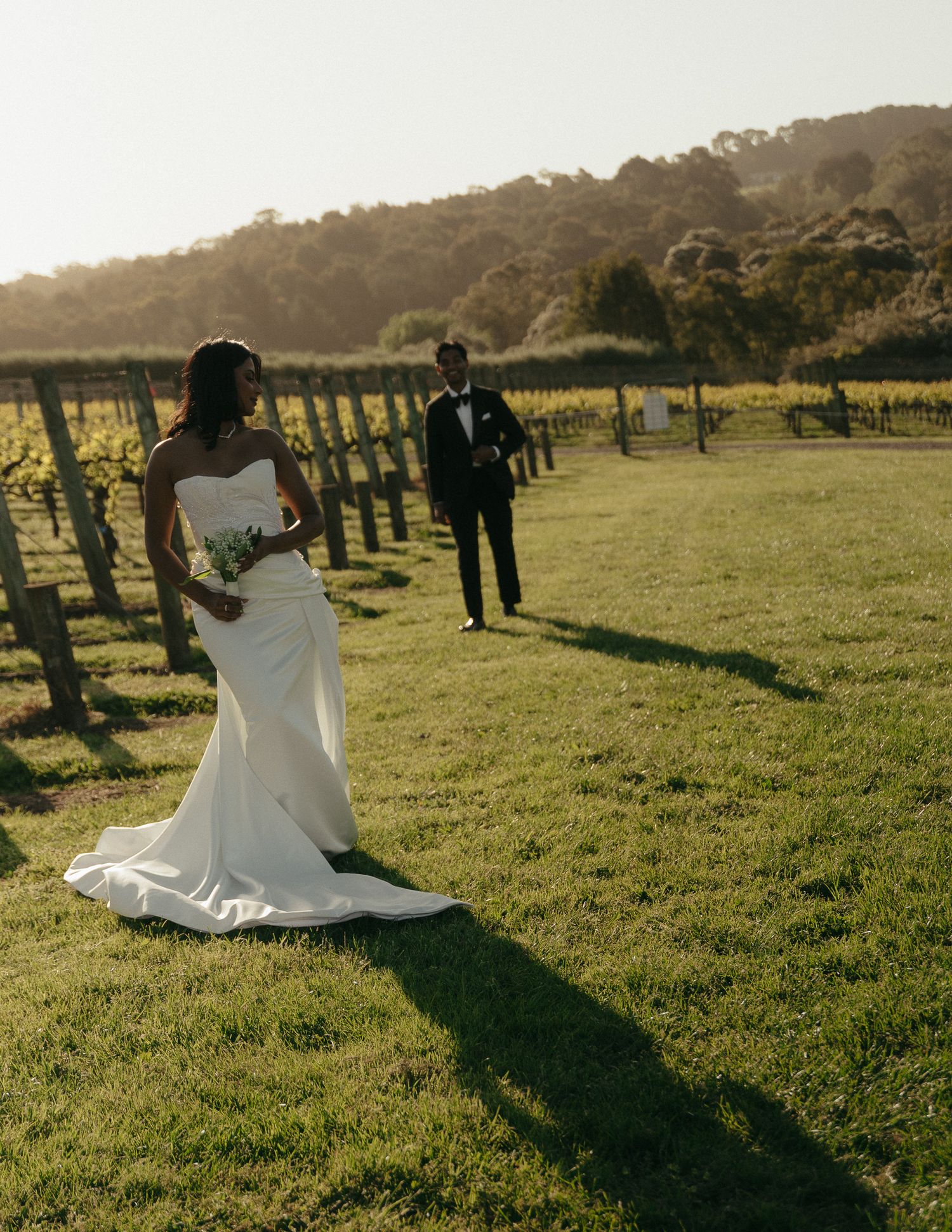A wedding dress flows elegantly across a sunlit grassy field during golden hour at an outdoor venue.