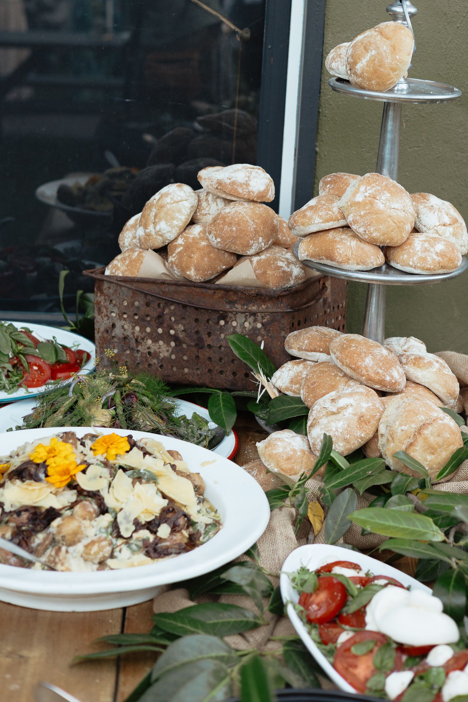 A display of fresh bread rolls and salads including a meat dish with eggs and fresh vegetables arranged on a rustic table.