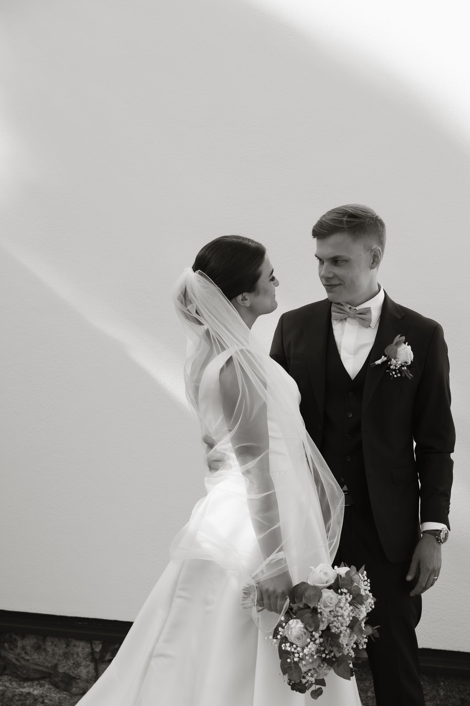 Romantic black and white portrait of a wedding couple against a light background.