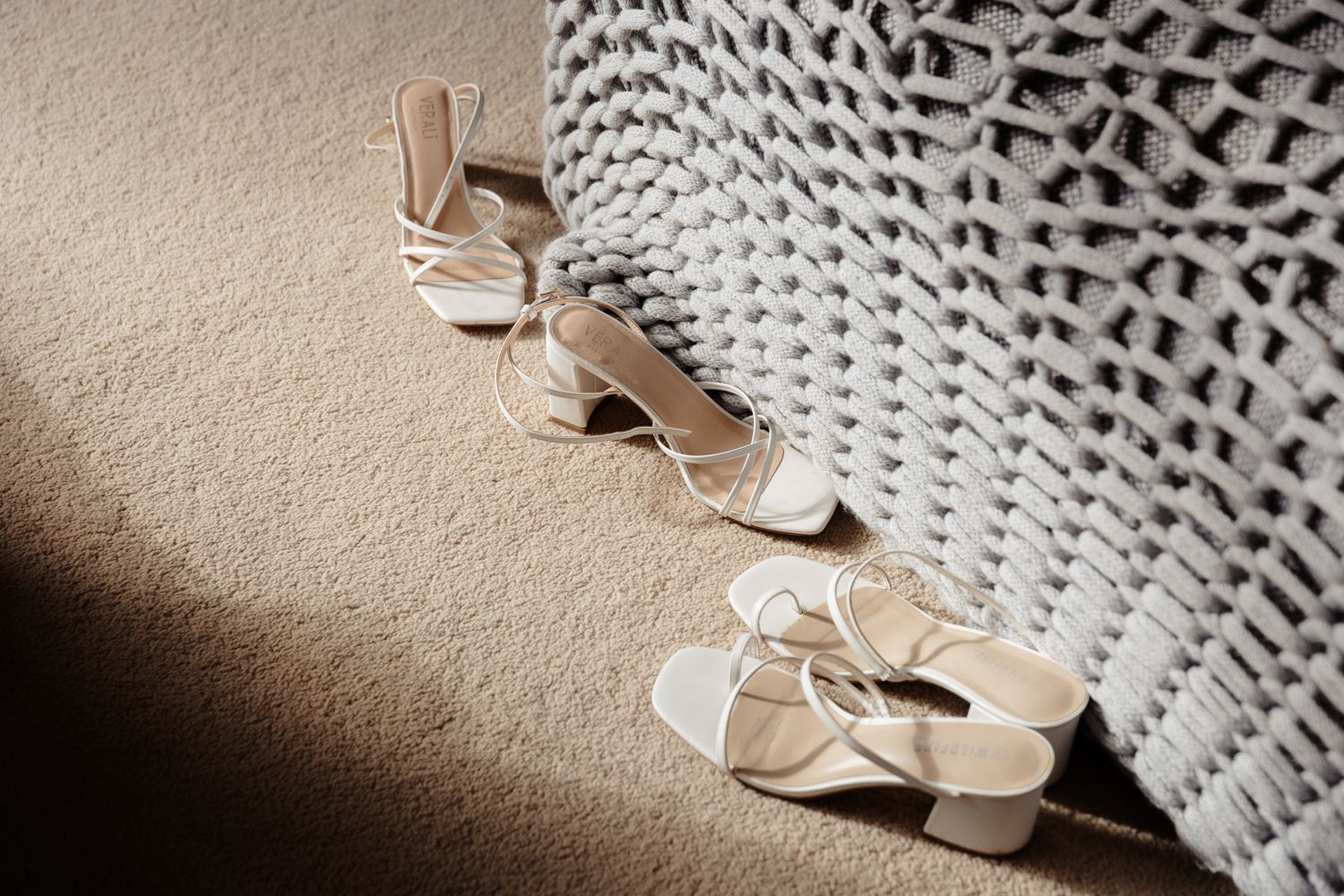 White ballet pointe shoes resting beside a knitted blanket casting dramatic shadows in natural light.