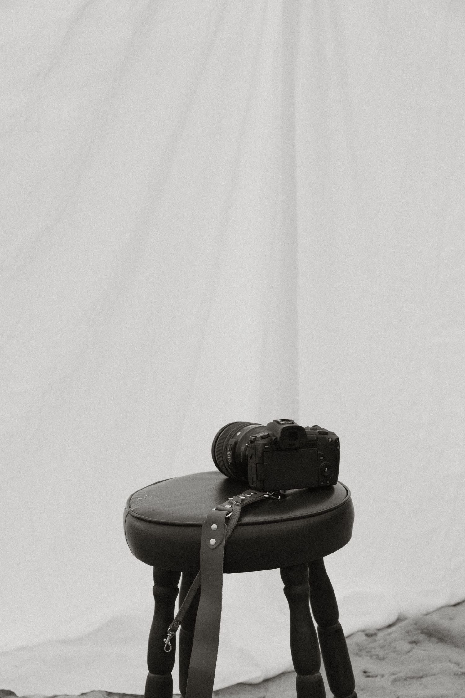 A black camera and lens sitting on a dark leather stool against a light gray background.