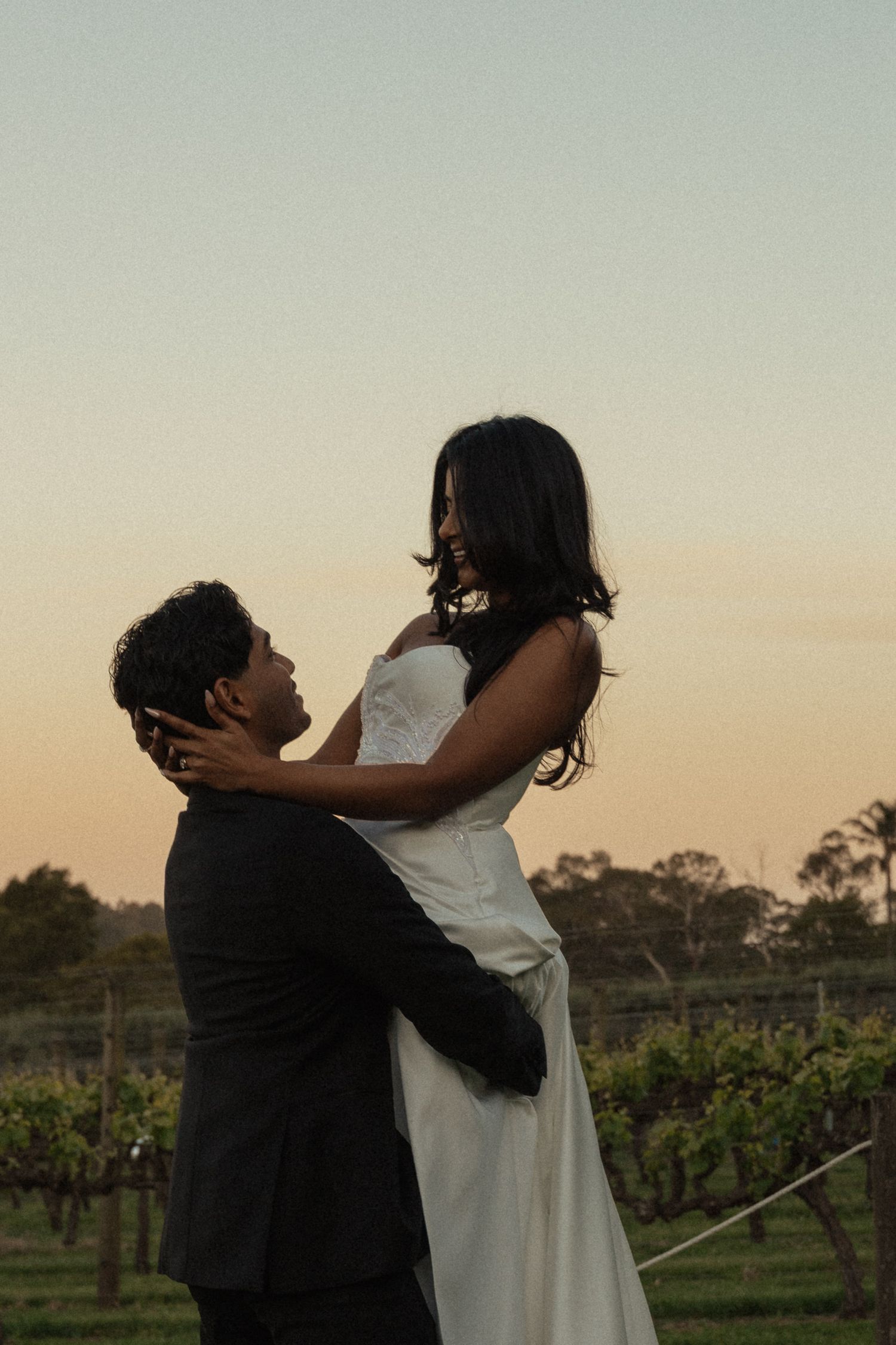 A romantic couple shares an intimate moment at sunset in a vineyard setting.