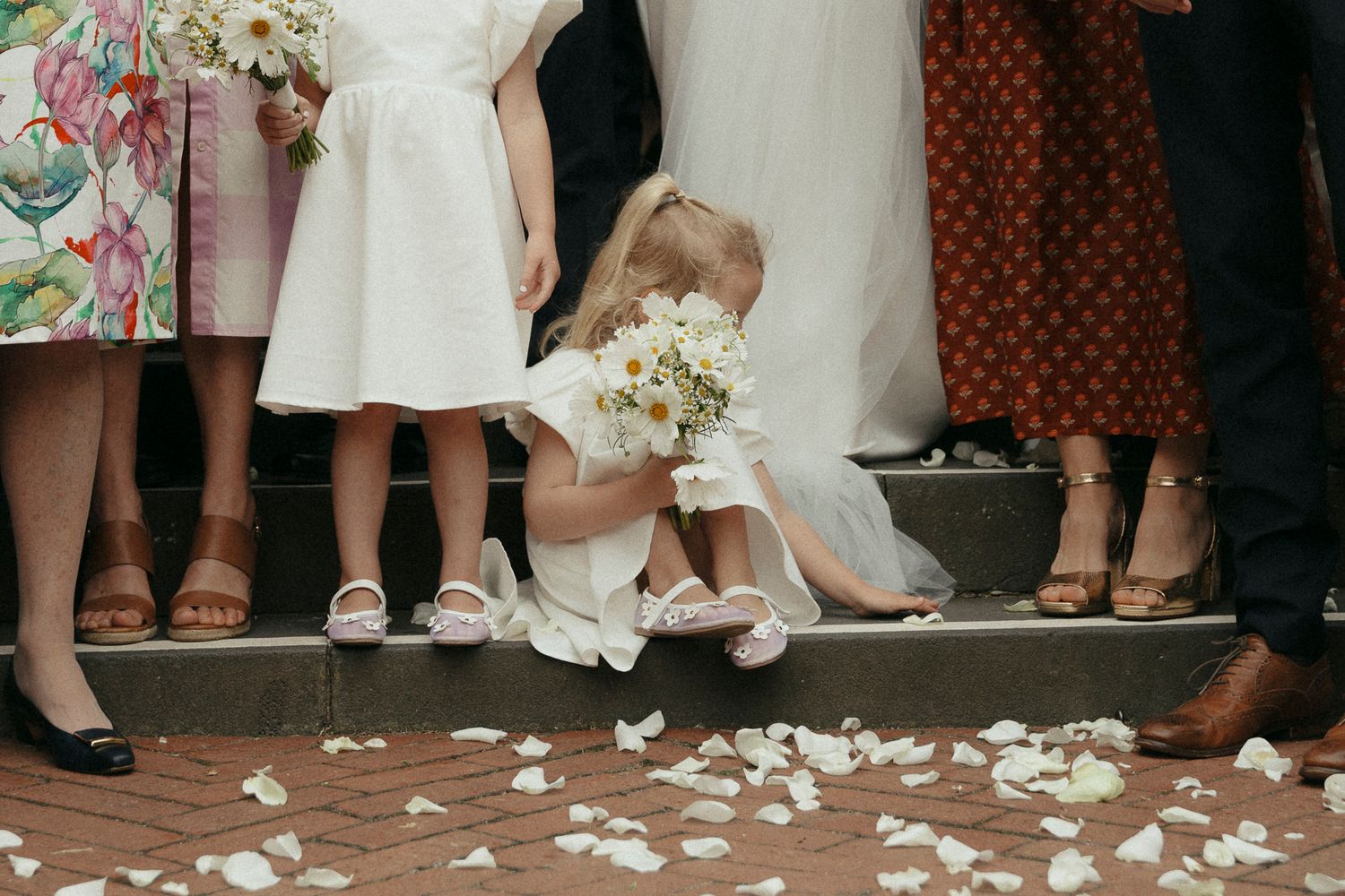 White flower petals scattered on steps with formal wedding attire and floral bouquet visible.