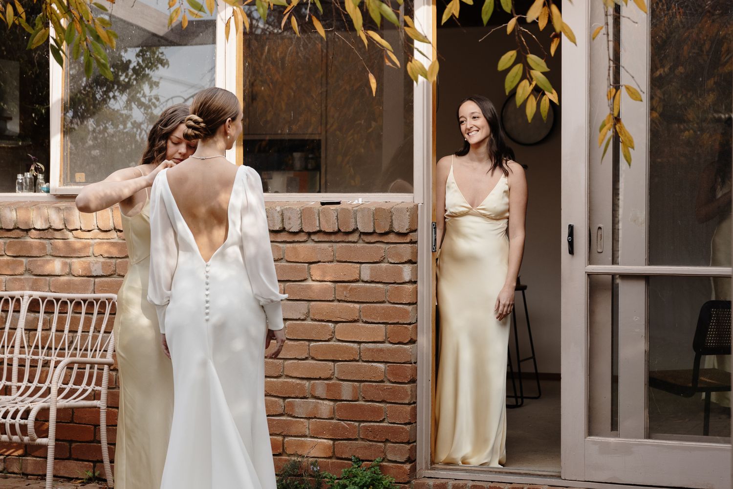 Two women in elegant silk wedding dresses in garden courtyard setting.