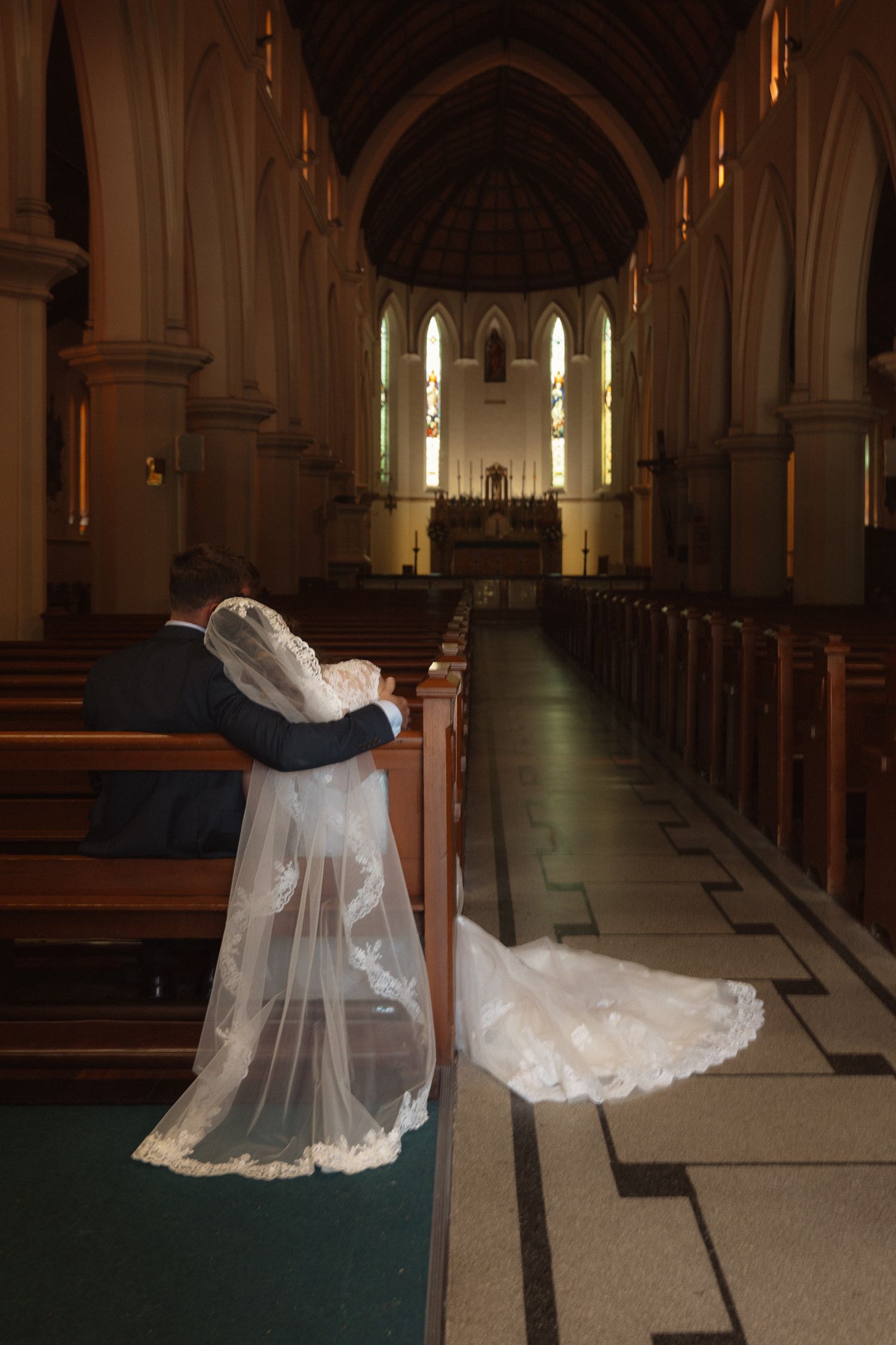 Wedding dress and veil draped over church pew in gothic cathedral with dramatic lighting.