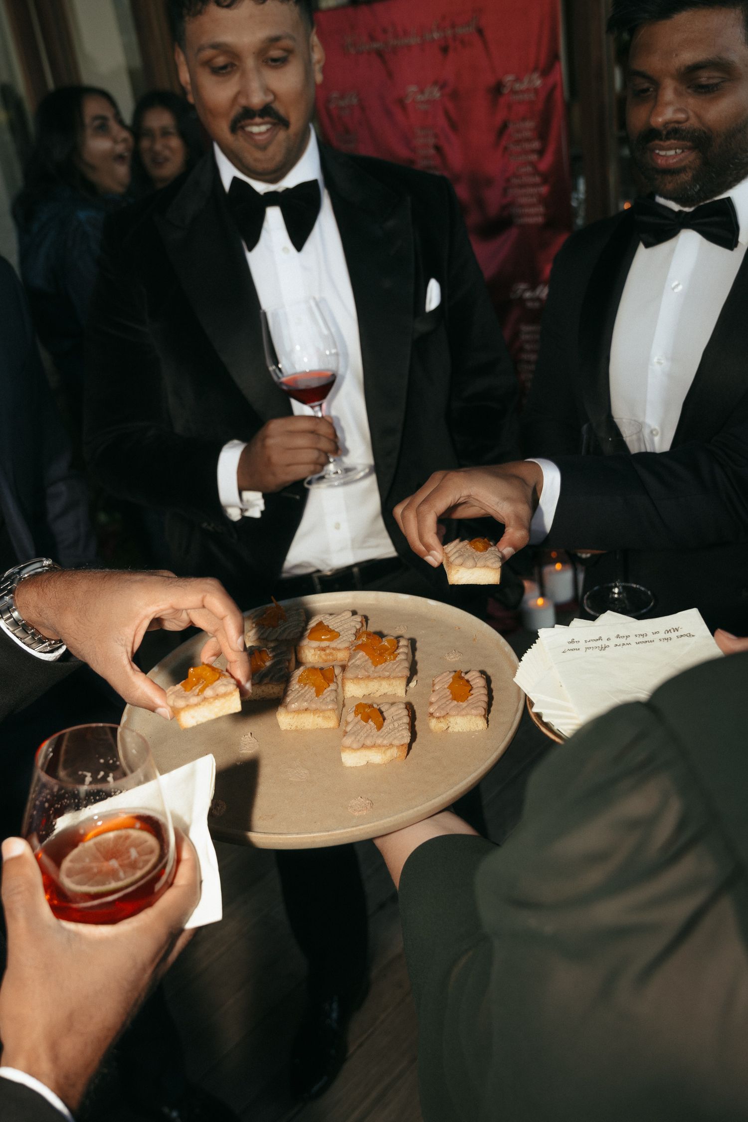 Guests in black tie attire share appetizers at an elegant reception.