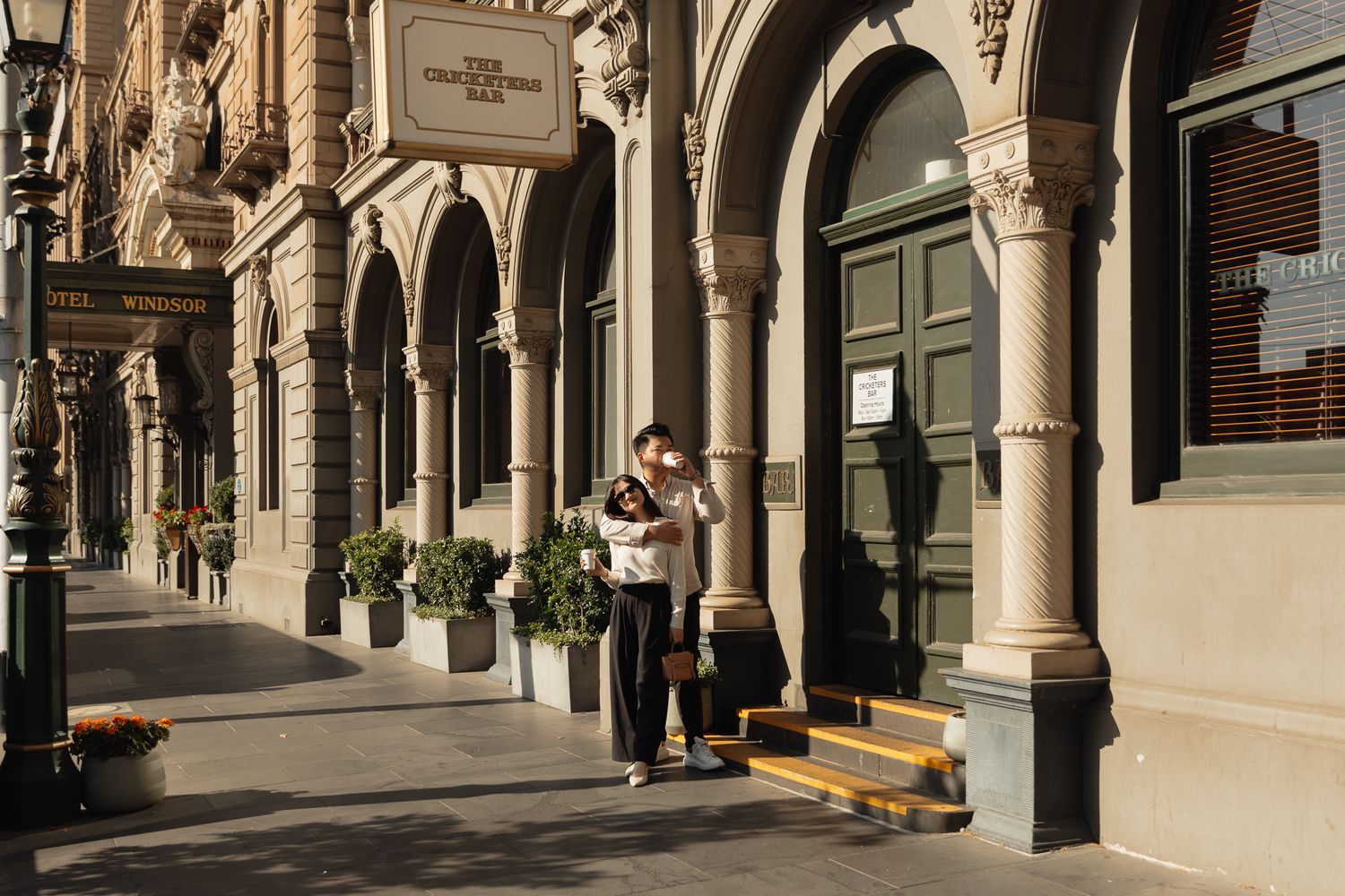 A couple embraces under ornate stone arches along a historic building facade.