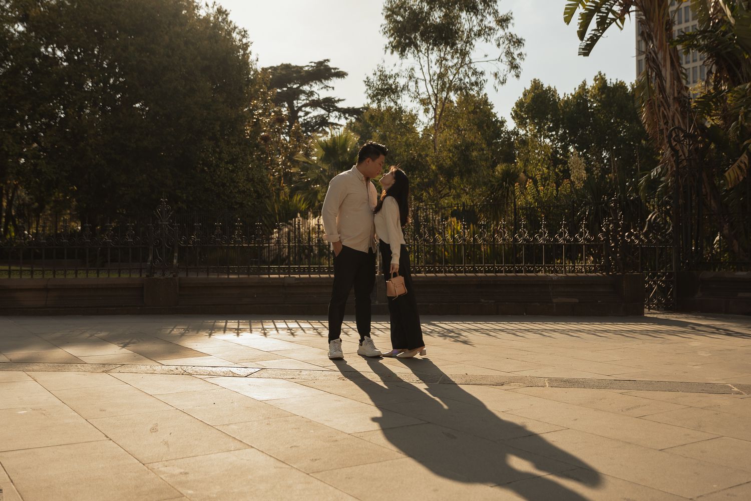 A couple stands together casting long shadows on a sunlit patio during golden hour at sunset.