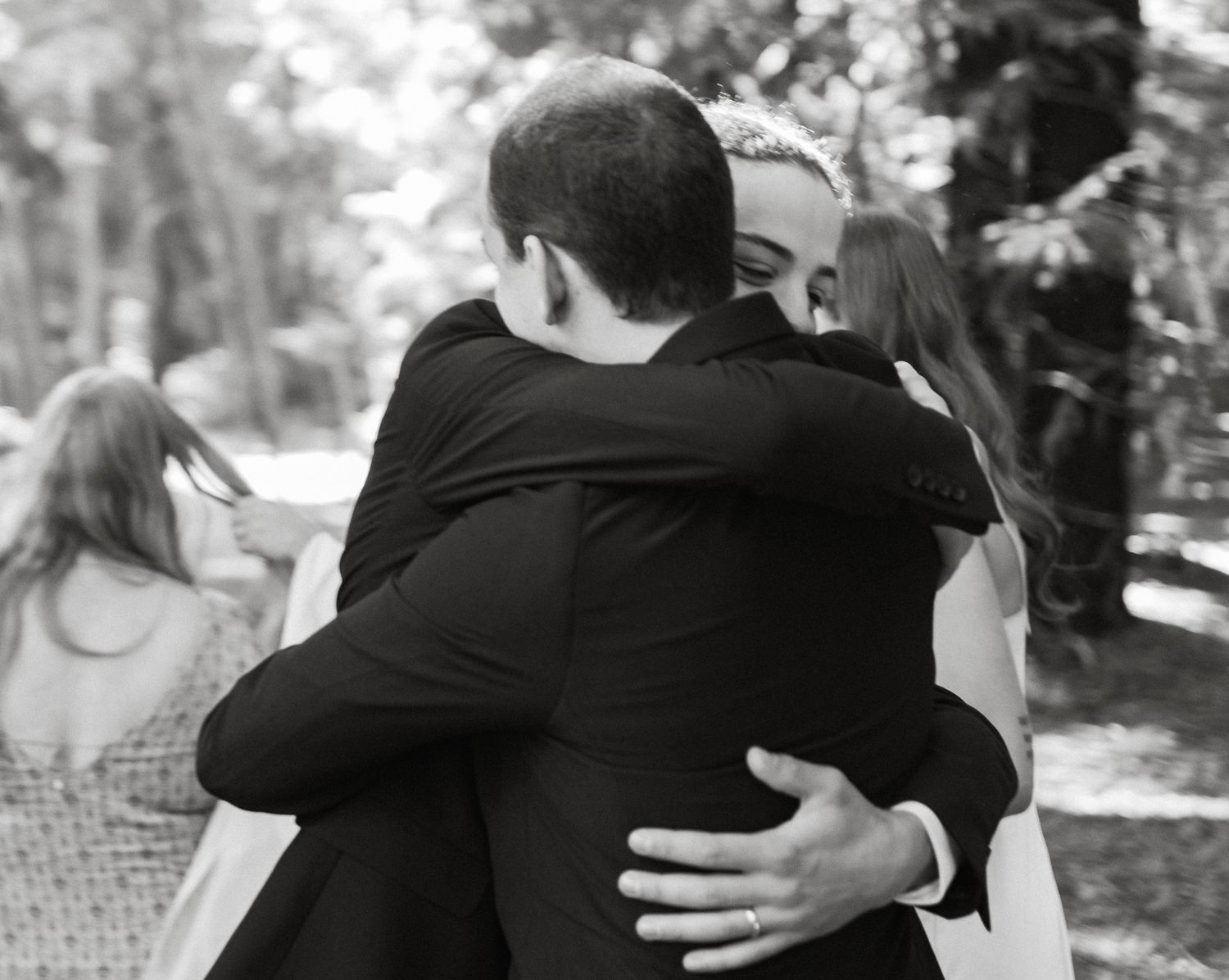 Two people embrace in an intimate black and white moment captured during what appears to be an outdoor gathering.