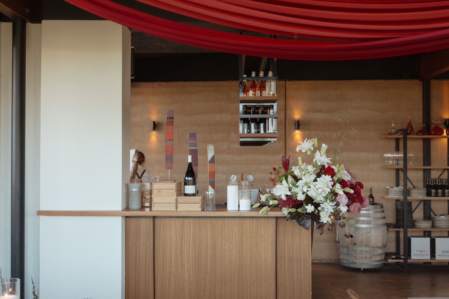 Modern restaurant interior with wooden walls, red ceiling drapes, and bar area visible in the background.