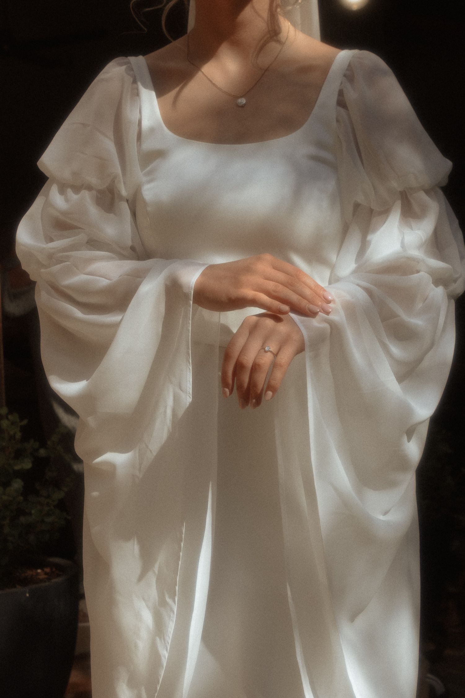Elegant white satin dress with billowing bishop sleeves and delicate neckline shown in soft romantic lighting.