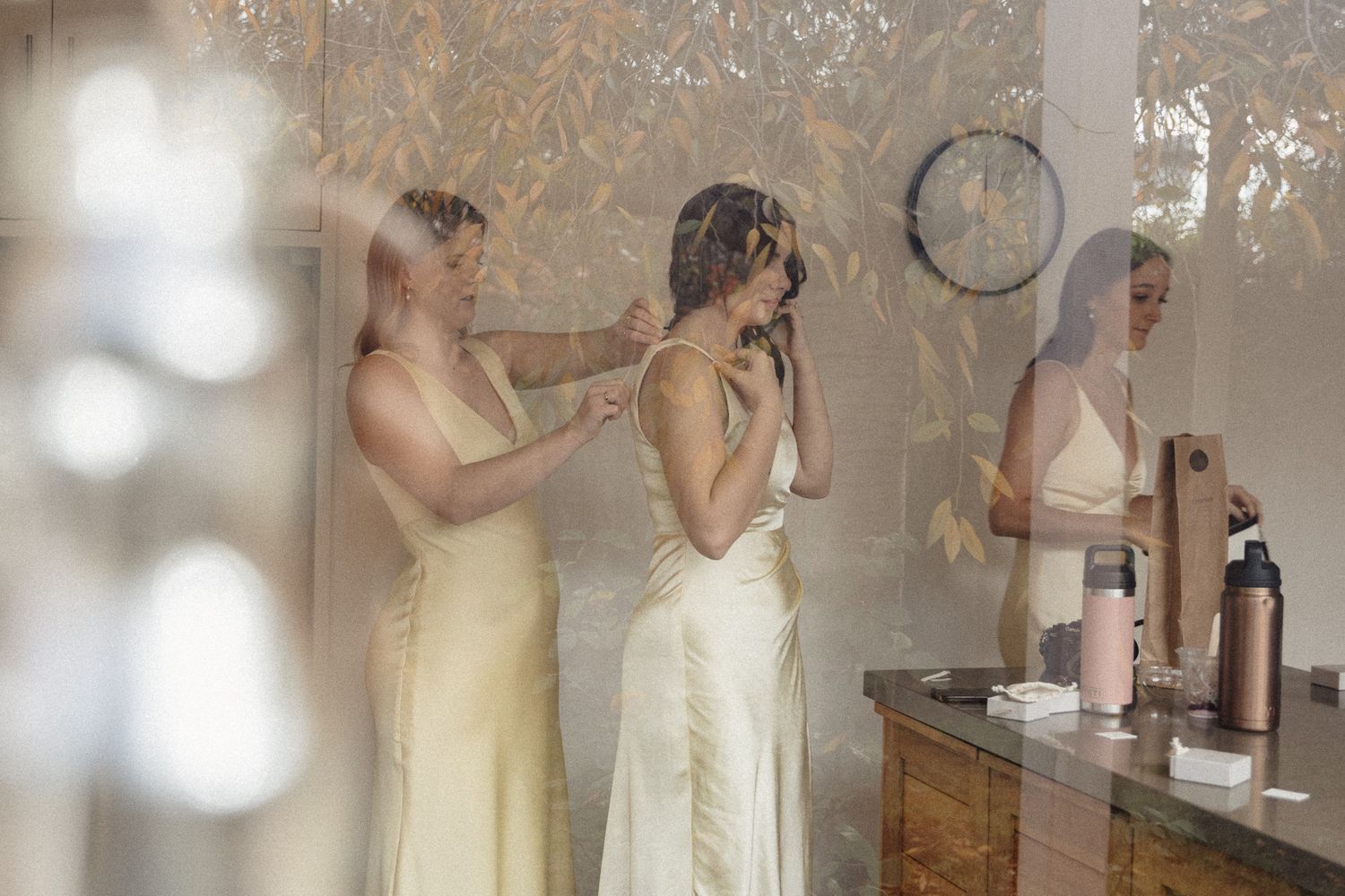 A bride getting ready in an elegant cream gown while looking in a mirror with her wedding party.