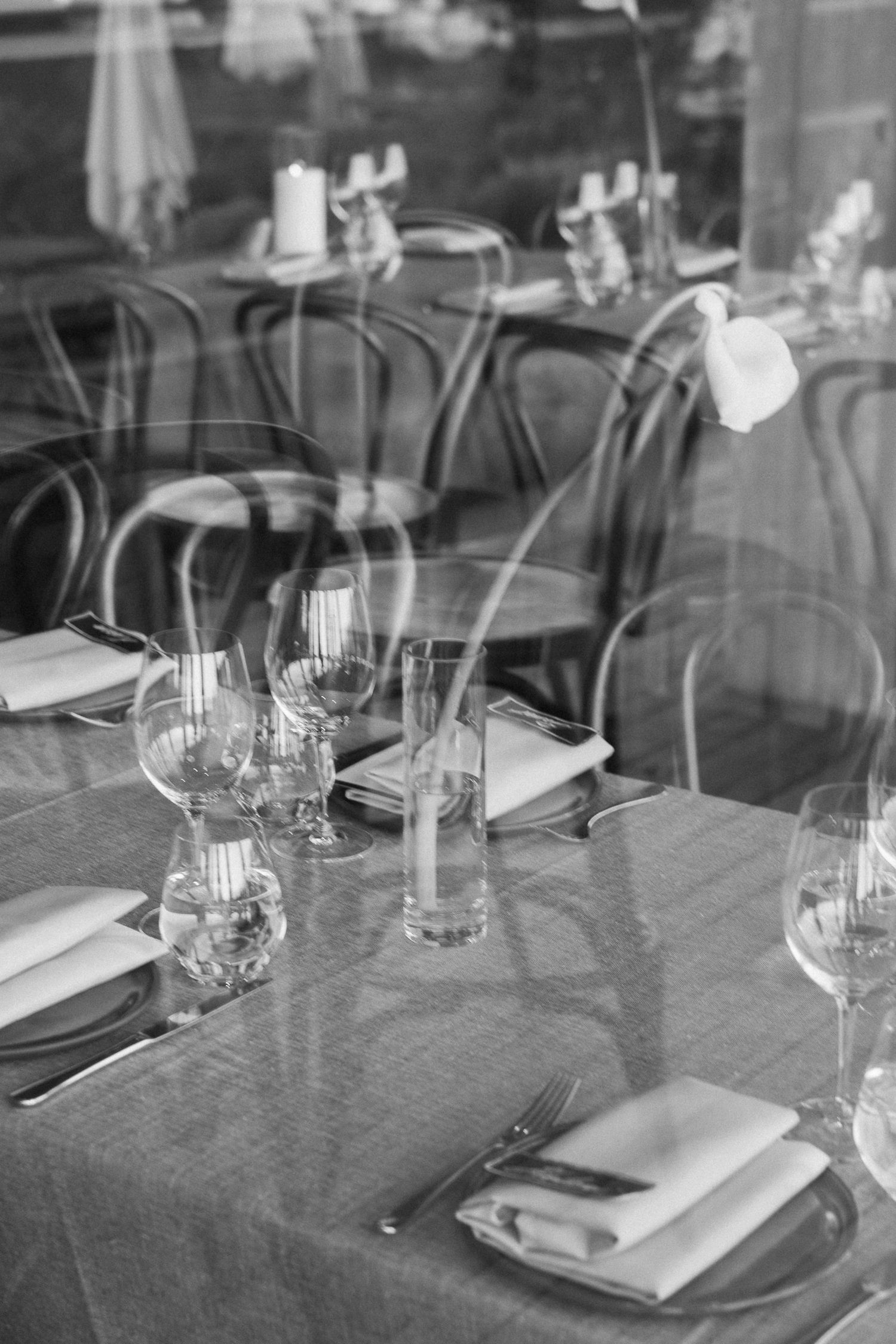 Elegant restaurant table settings with wine glasses and white napkins on gray tablecloths in black and white photography.