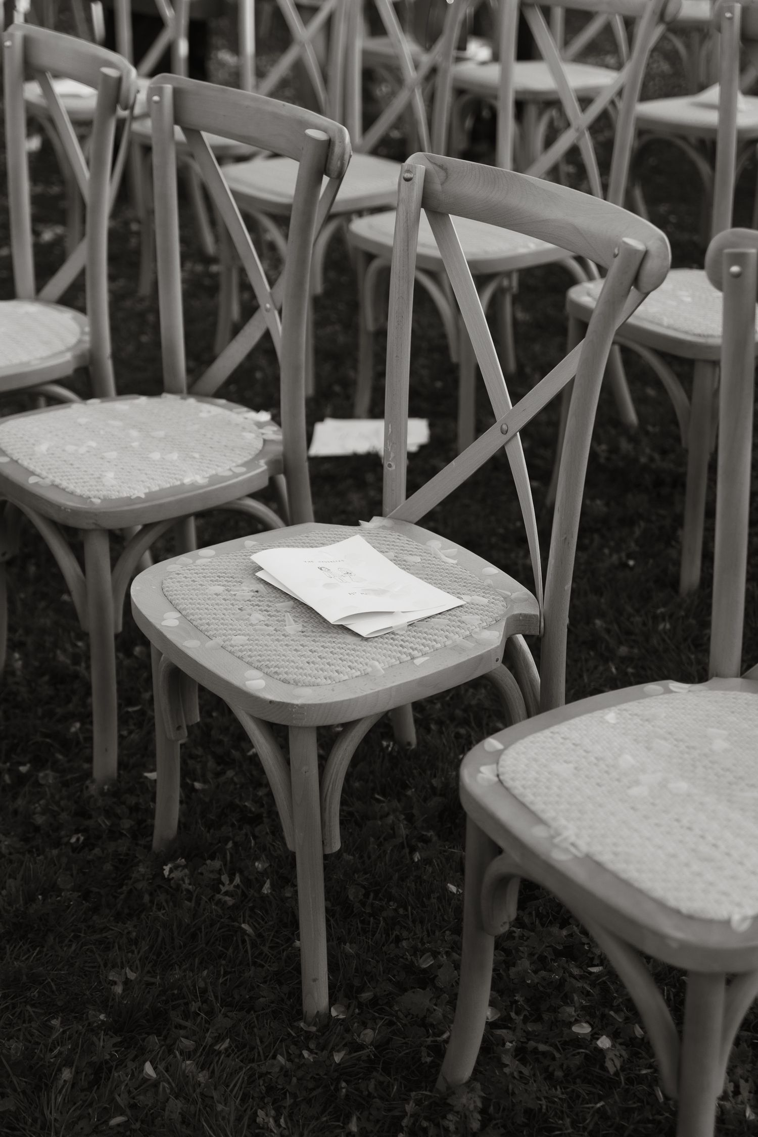 A black and white photo of vintage bistro chairs arranged in rows with a piece of paper resting on one seat.