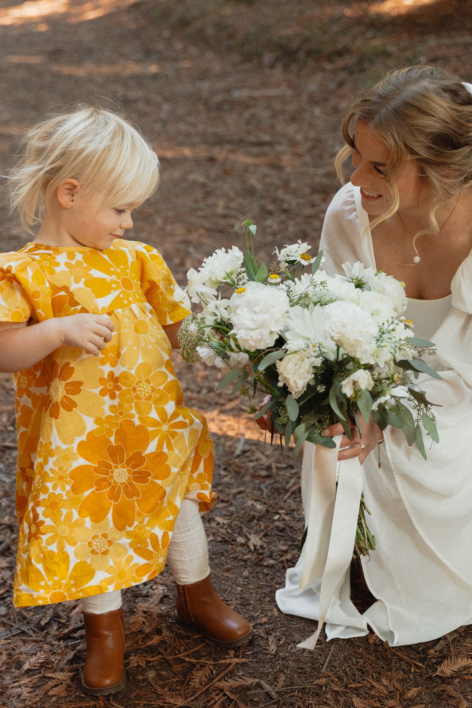 A sweet moment at a wedding with white flowers as a small child in a bright yellow floral dress stands with a bride.