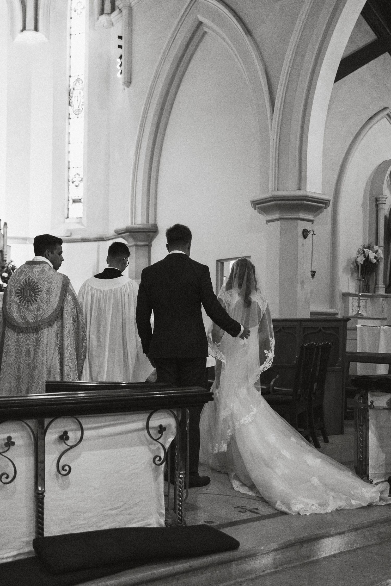 Black and white photograph of couple at wedding ceremony with clergy members at altar in traditional church interior.