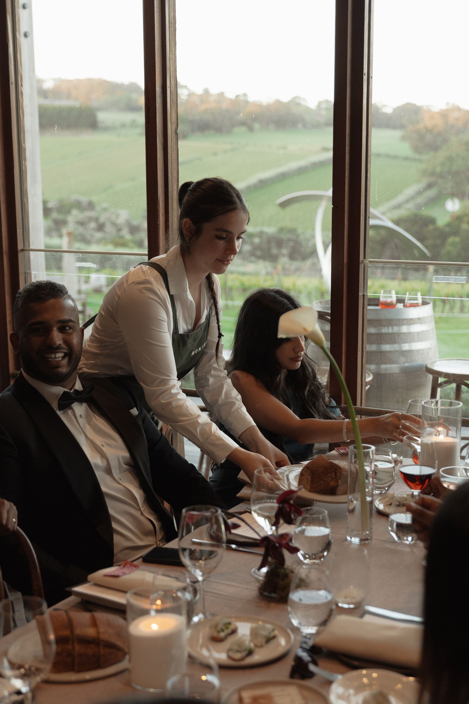 Guests seated at a formal dining table with panoramic window views of rolling hills.