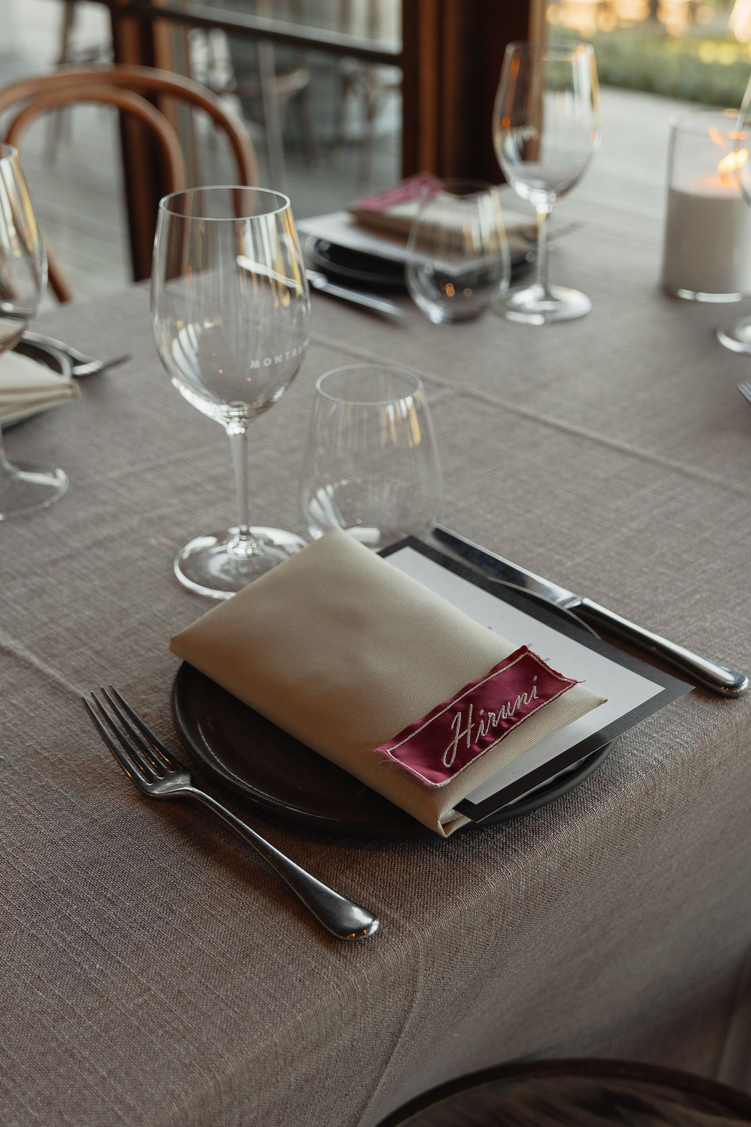 Elegant table settings with white napkins, silverware, and burgundy menu cards arranged on a gray linen tablecloth.