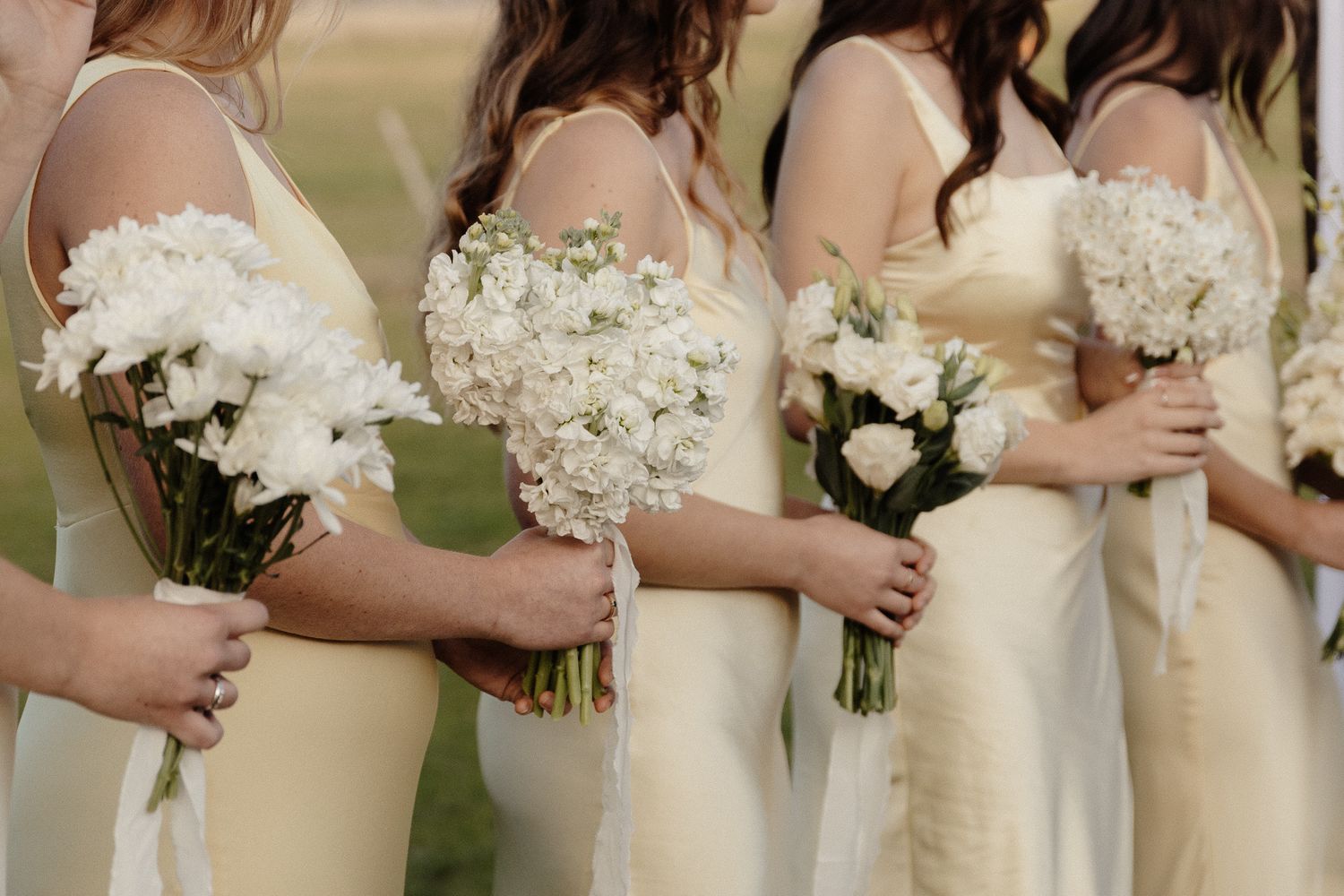 Row of bridesmaids in cream-colored dresses holding white floral bouquets.