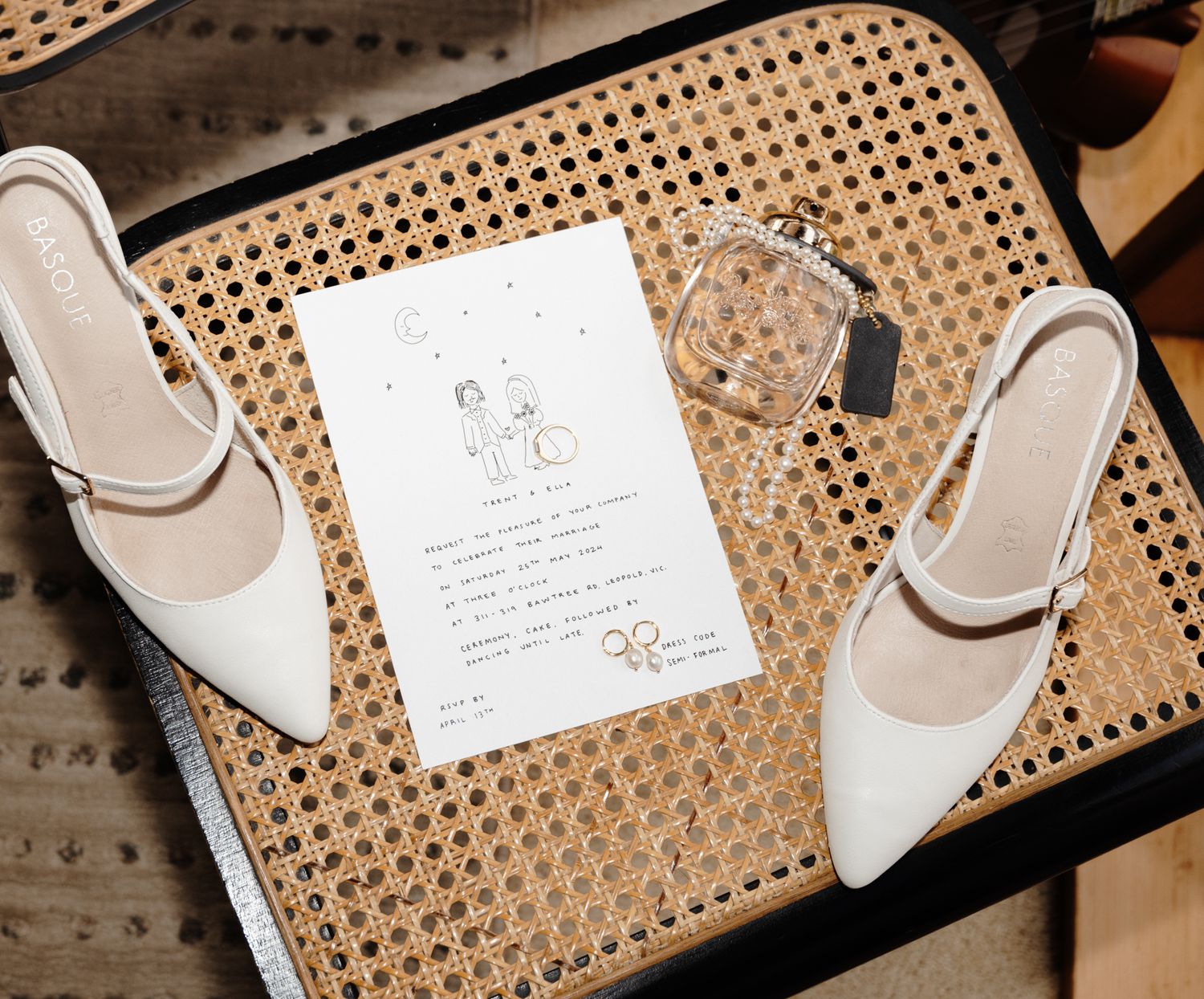 Wedding invitation card and white bridal shoes arranged on rattan textured furniture.