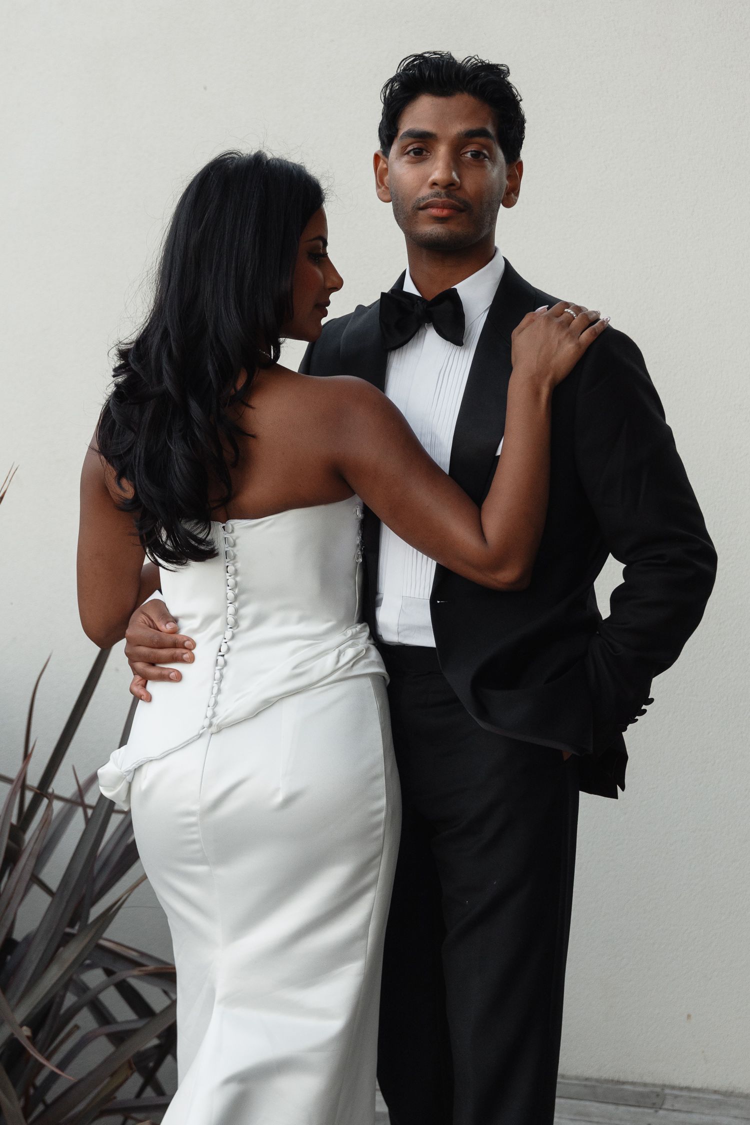 A couple in formal attire, with the woman in a white dress and man in black suit, posing together in multiple shots.