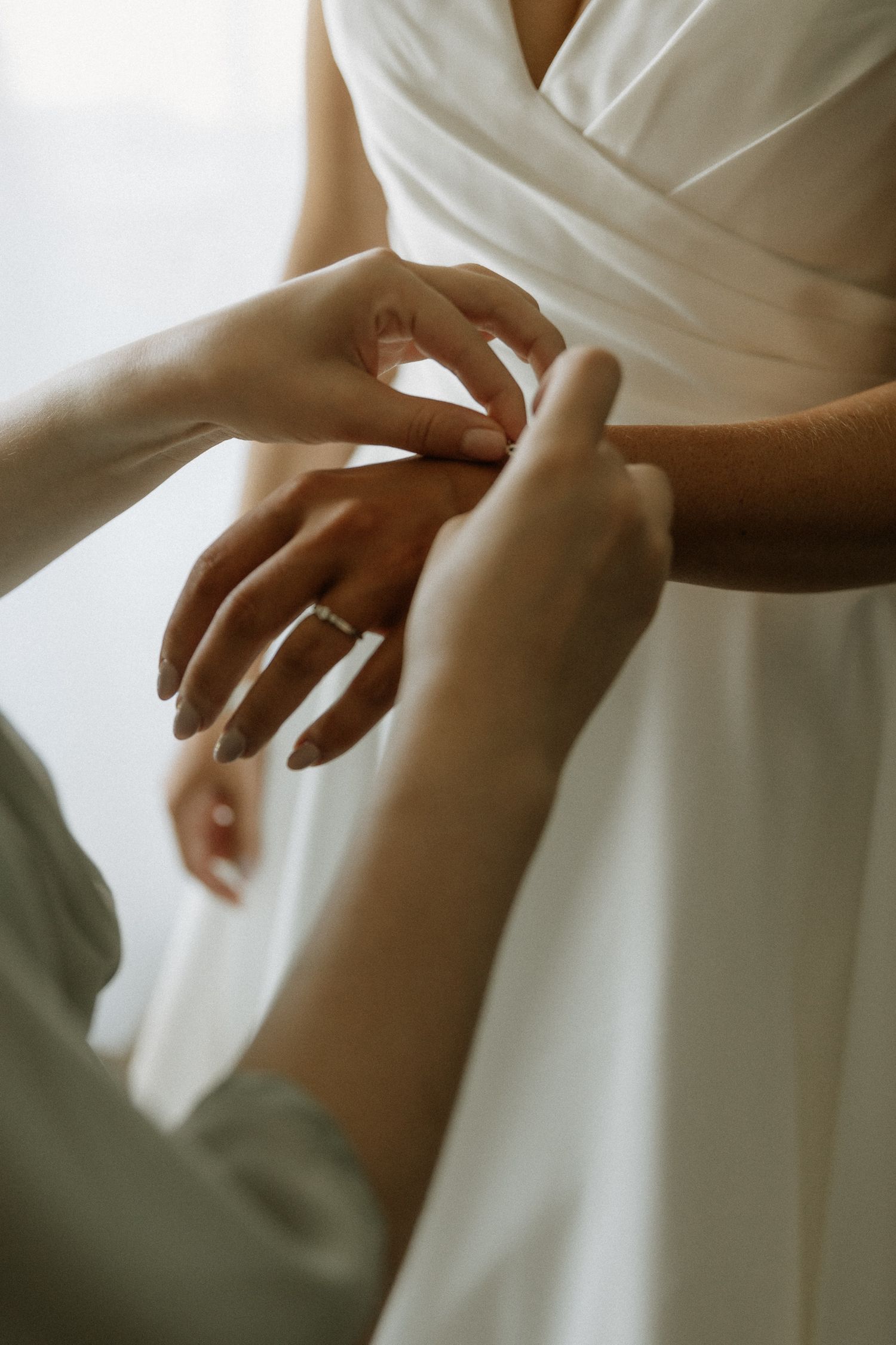 Hands adjusting jewelry on a person wearing a white wedding dress.