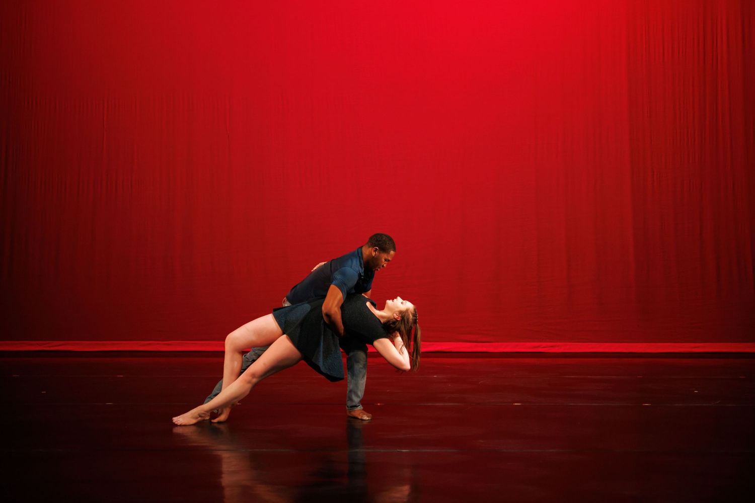 Two dancers on stage performing a passionate dip against a vibrant red backdrop. Live performance photo by Sasy Cassie.