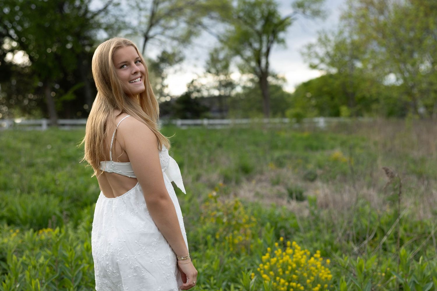 Woman in white dress poses outdoors in a field of yellow wildflowers during spring.