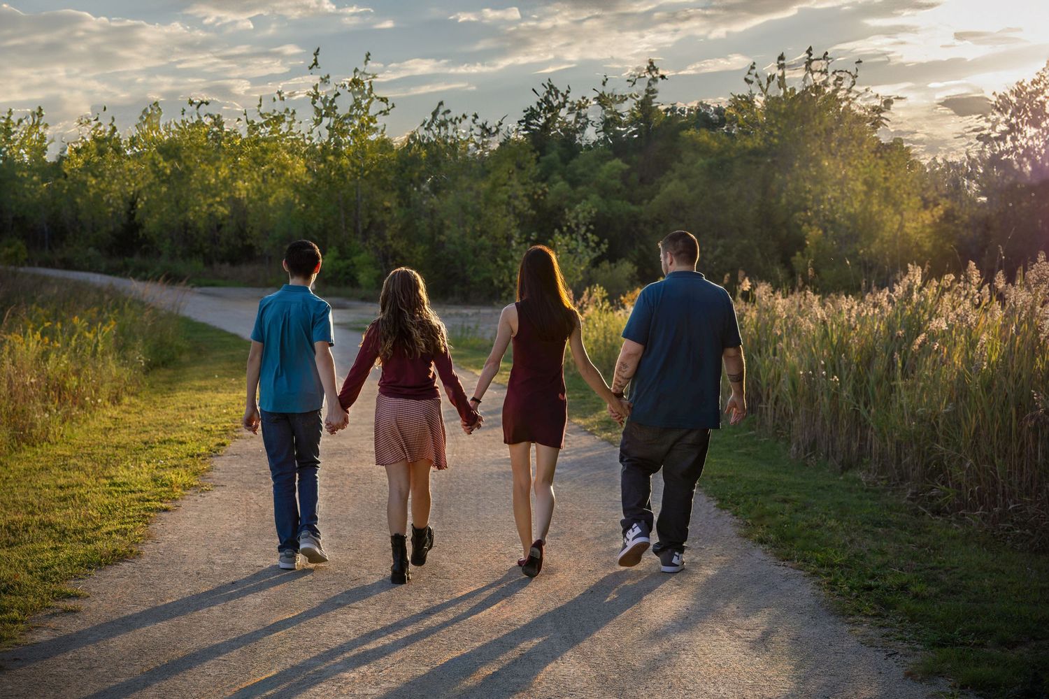 A group of people walking together on a nature trail at sunset, viewed from behind.