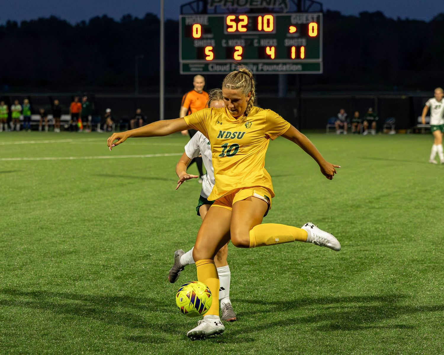 Soccer goalkeeper in yellow uniform diving to make a save during nighttime match under stadium lights.