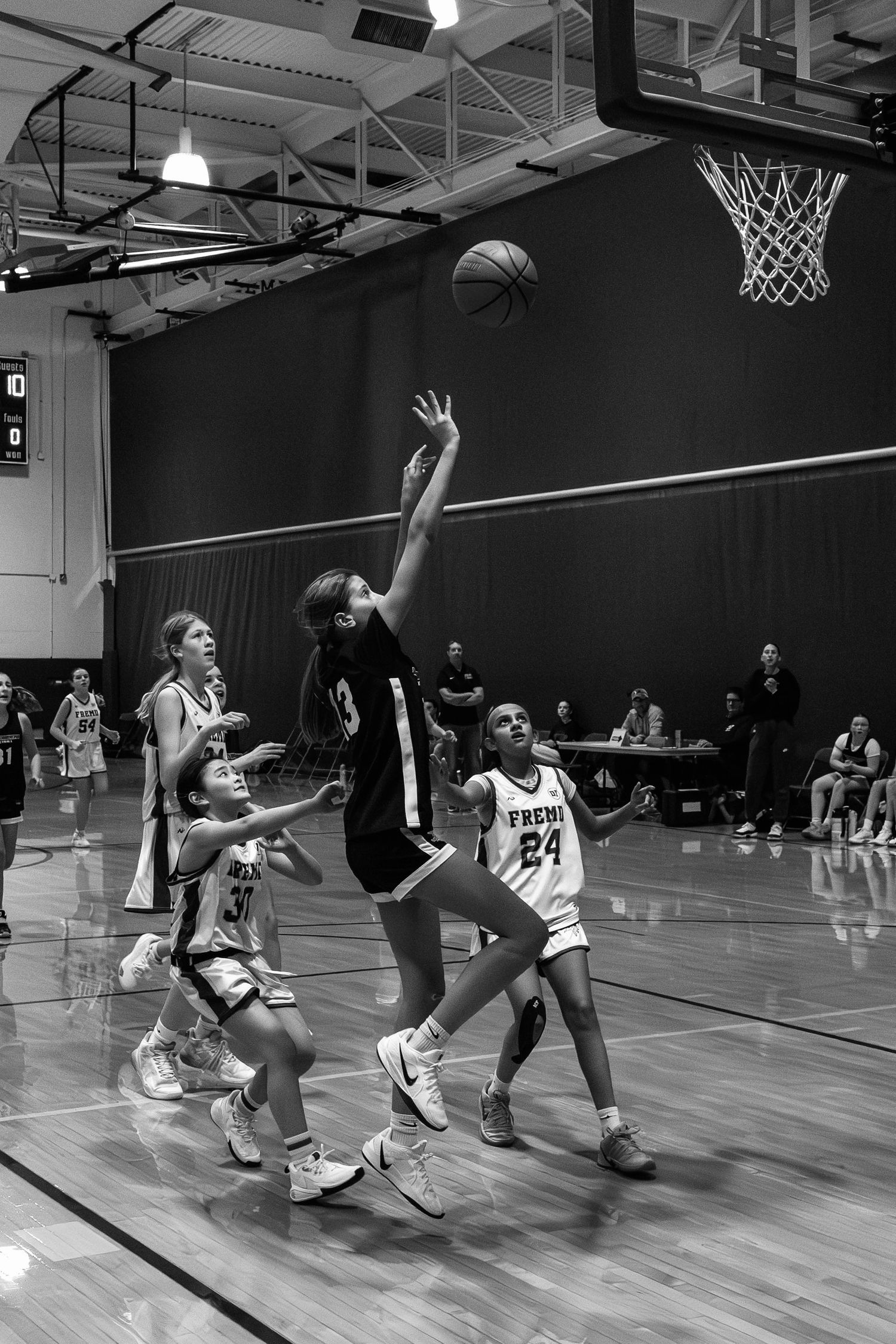 Girls basketball player leaps for a layup during an indoor game, with defenders watching in black and white photo.