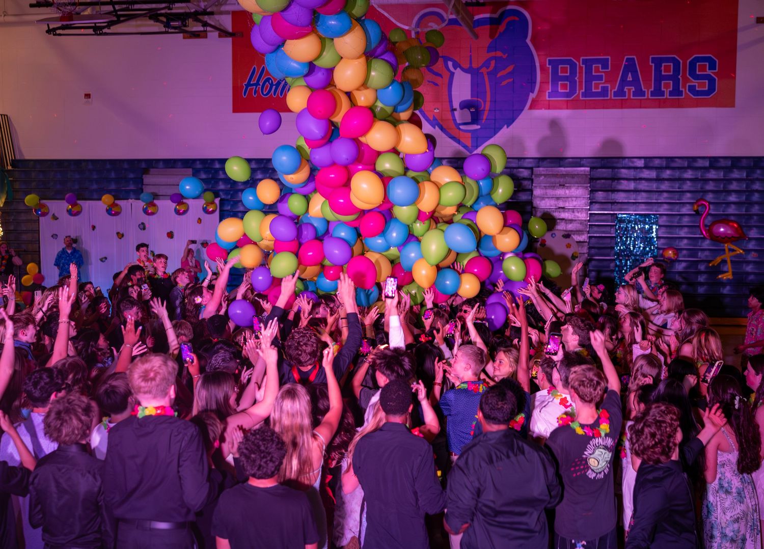 Students celebrate at a Bears school dance with colorful balloons dropping in a gymnasium.