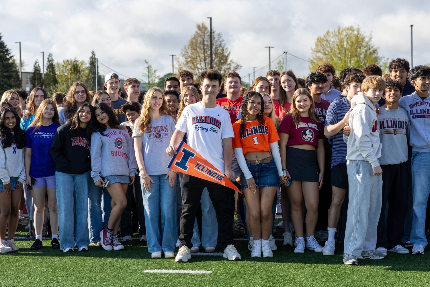 Large group of college students posing together on a sports field, many wearing University of Illinois apparel.