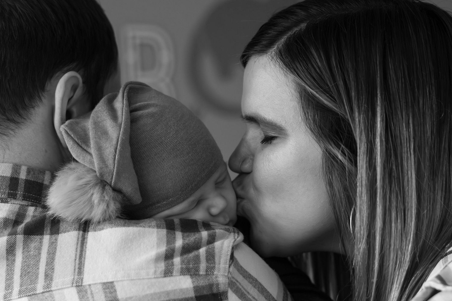 Black and white photo of a mother tenderly kissing her newborn baby held by father.