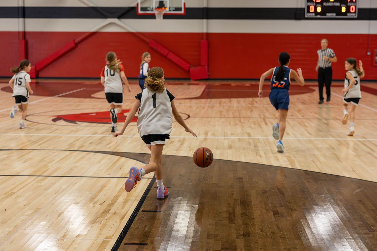 Girls playing basketball in a red and white gymnasium during a youth league game.