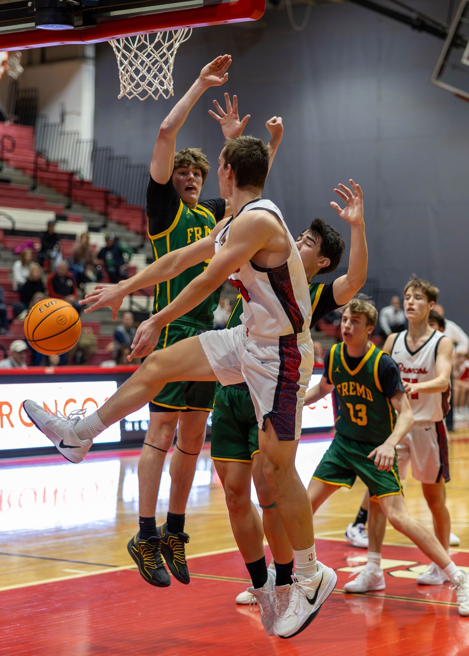 High school basketball players in green and white uniforms compete for a loose ball near the basket during an intense game.
