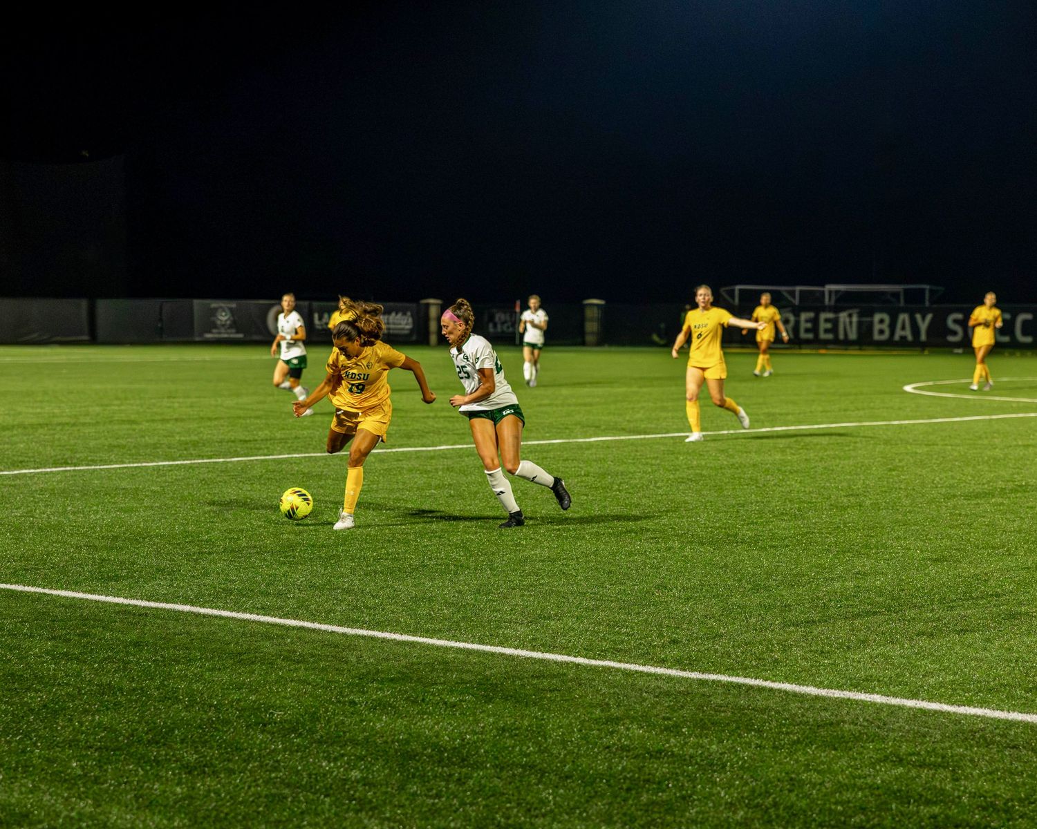 Soccer players compete on an illuminated green field during a nighttime match.