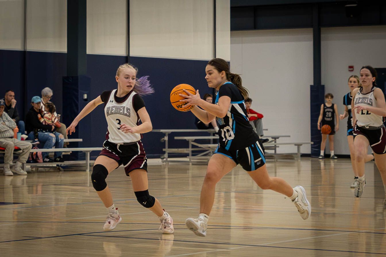 Basketball players compete in an intense indoor game with one player dribbling past a defender.