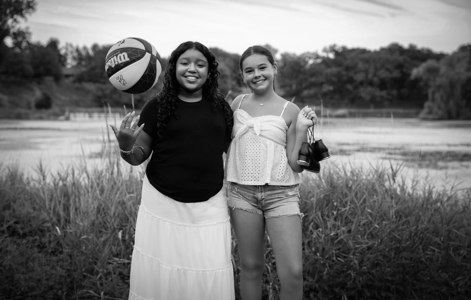 Group embraces and smiles together on sunny day outdoors in black and white photography.