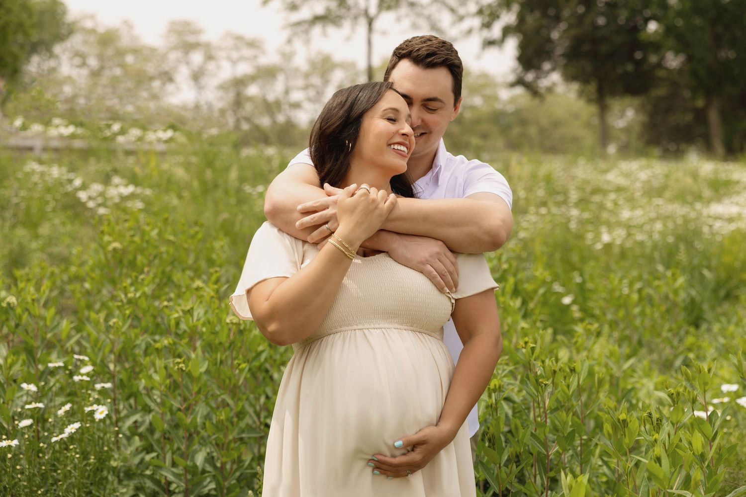 A couple shares a tender embrace in a wildflower meadow, with the pregnant woman cradling her baby bump.