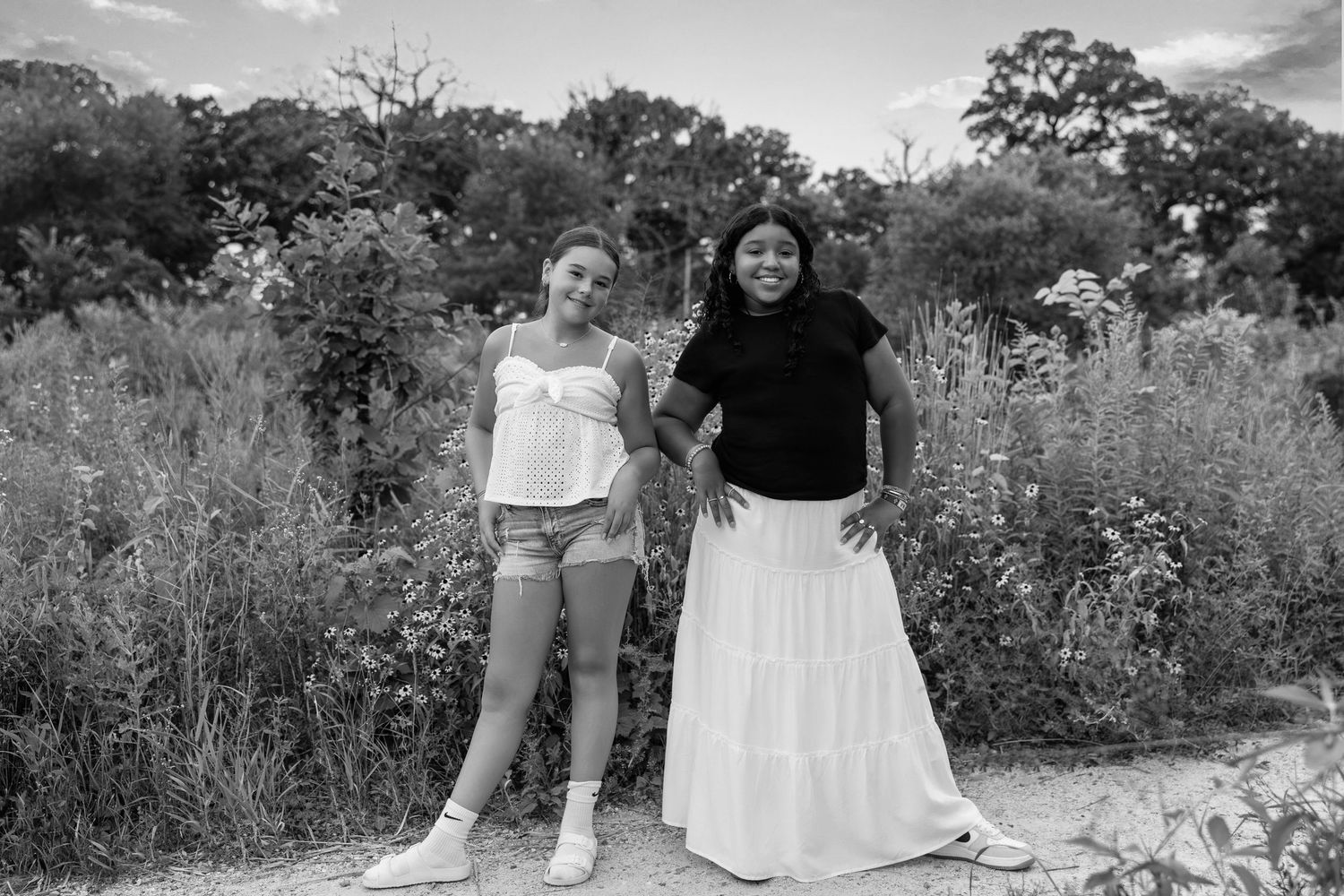 Friends enjoying a casual photoshoot on a wooden bridge with wildflowers in the background.