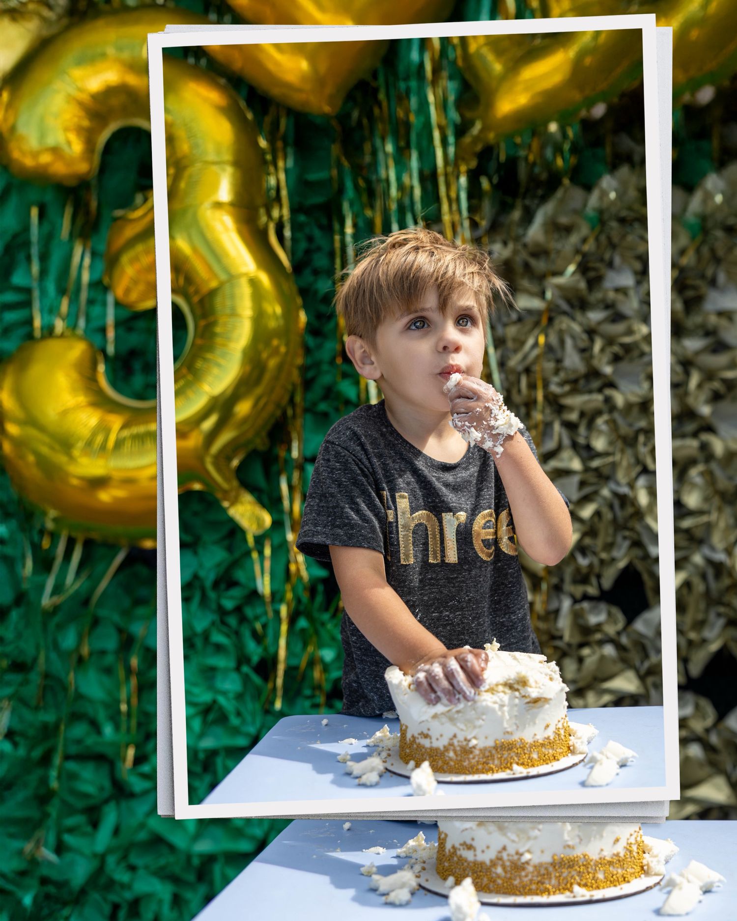 A young boy celebrates his 3rd birthday, eating cake at a decorated table with gold number balloons and green backdrop.