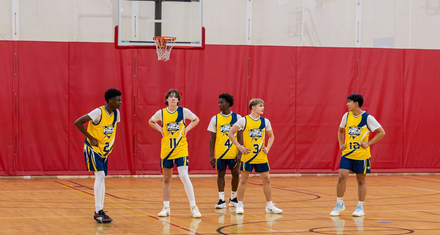 Five youth basketball players in yellow uniforms stand on an indoor court during a practice session.