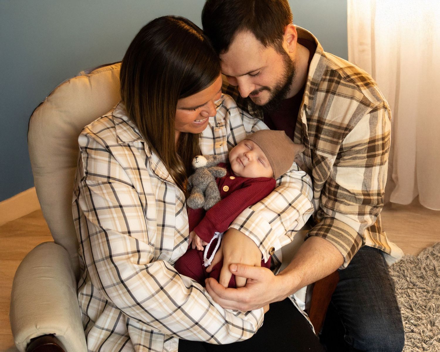A couple in matching plaid shirts lovingly gazes at their newborn baby in a cozy home setting.